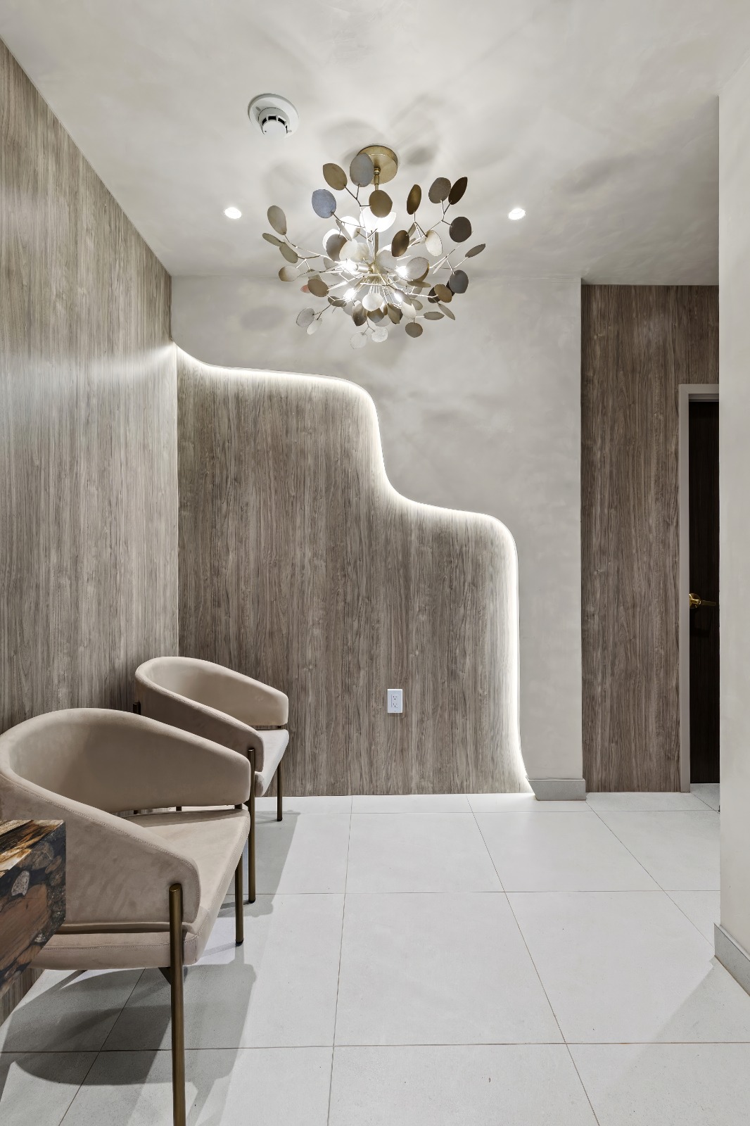 Waiting area with brass sputnik chandelier and LED cove lighting behind curved wood wall